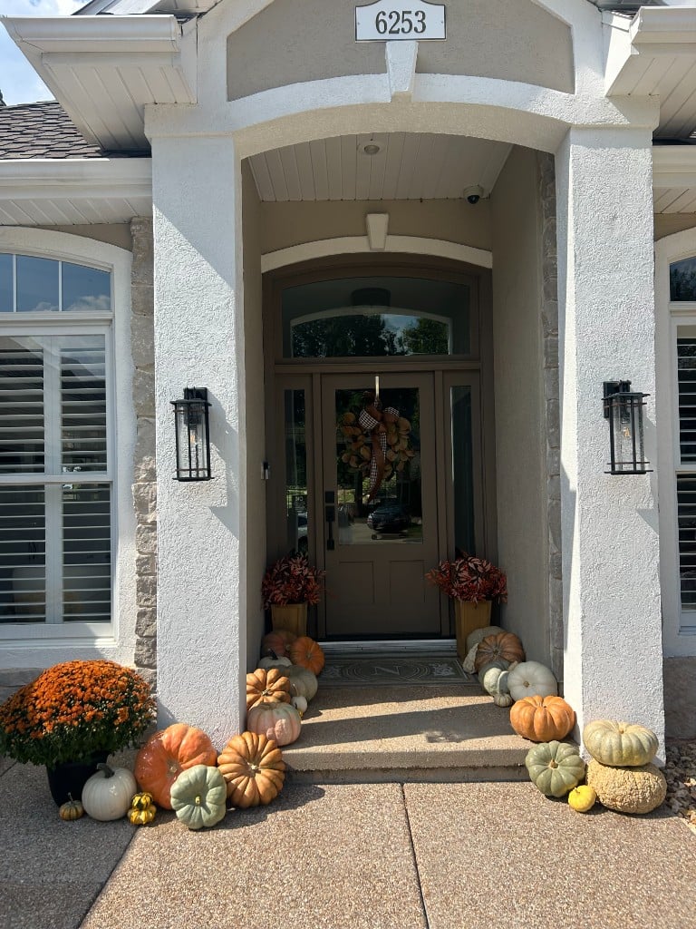 An arched stucco entryway lined with pumpkins and orange mums