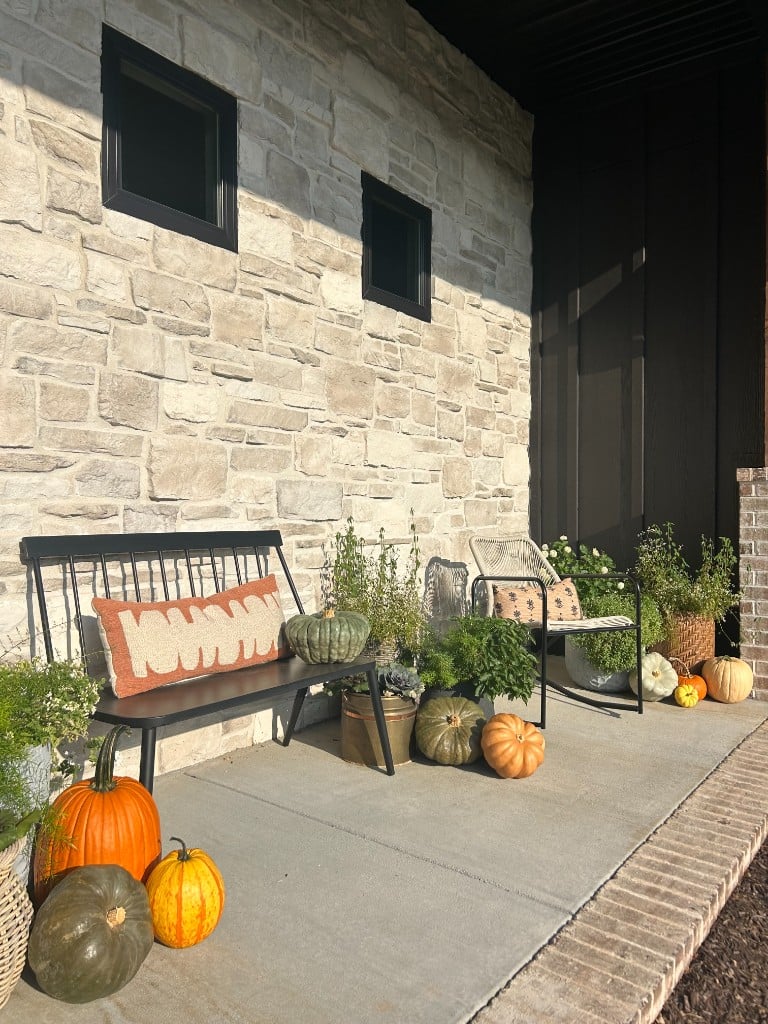A porch bench layered with pillows, mums, and heirloom pumpkins